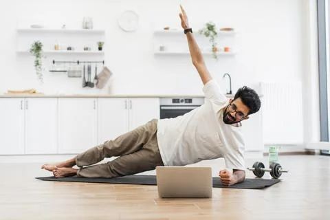 Man practicing side plank exercise in modern kitchen with laptop and equipment 스톡 사진
