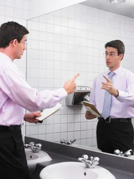 Man practicing speech in office washroom mirror Stock Photos