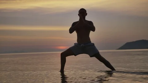 Man practicing warrior pose in the sea during sunset Stock Footage 75290790