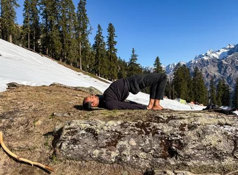 Man practicing wheel pose yoga on mountain with snow and pine forest backgrou Foto stock
