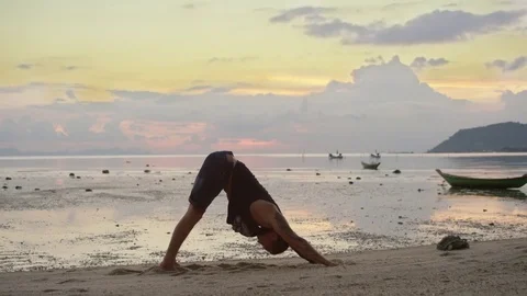 Man practicing yoga on the beach at sunset Stock Footage 74770035