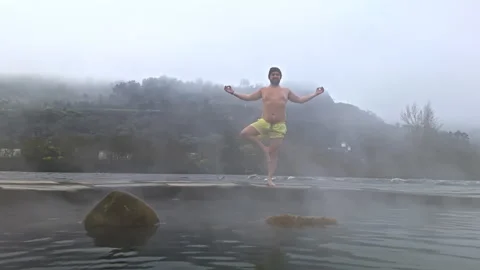Man practicing yoga by hot spring in foggy landscape Stock Footage 280257996