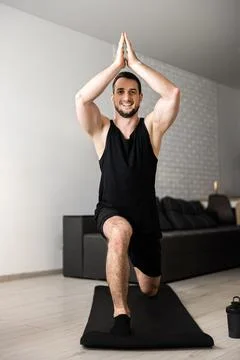 Man practicing yoga indoors doing Warrior one on black mat. Muscular young man Stock Photos