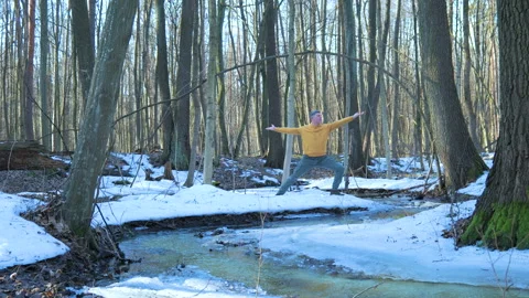 Man practicing yoga near forest stream on melting snow in early spring Stock-Footage 334921577