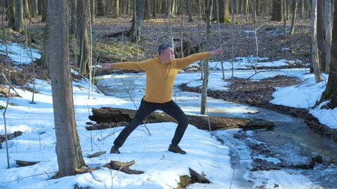Man practicing yoga pose in winter forest near frozen stream 库存影片 334372677