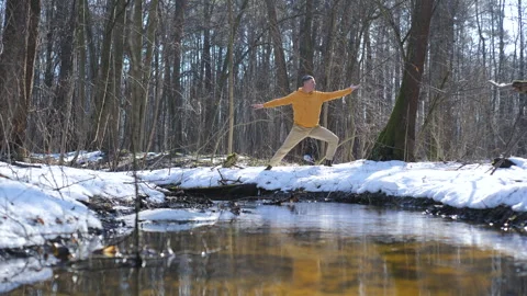 A man practises yoga by a forest stream on the snow in a snow-covered forest in Stock Footage 346282062