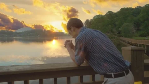 Man in prayer at sunset by lake Stock Footage 153110831