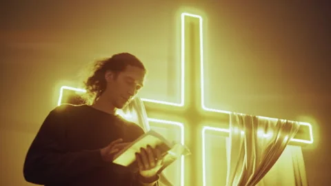 Man in Prayerful Reading, Lit by Glowing Christian Cross Stockbeeldmateriaal 327207366