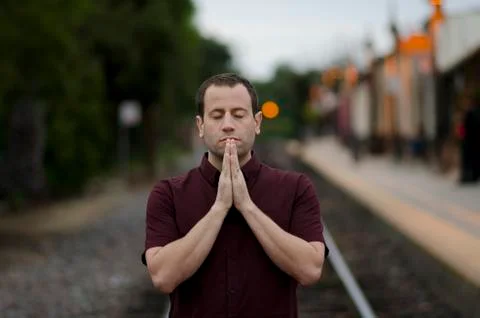 Man praying alone at a train stop. Stock Photos
