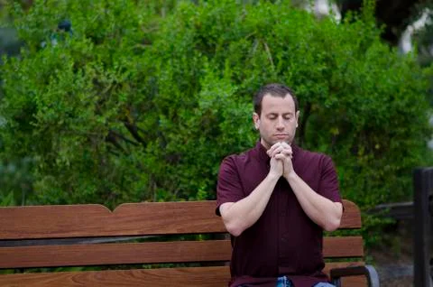 Man praying on a bench outside alone. Stock Photos