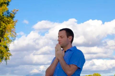 Man praying with the clouds and trees in the background. Foto stock