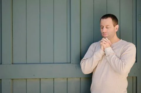 Man praying with hands clasped in front of a green wooden garage door. Stock Photos