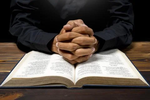 Man praying with his hands on a opened holy bible on wooden table. Symbol o.. Foto stock