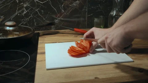 Man prepares dinner in the kitchen in the evening, cuts a tomato into slices on Stock Footage 155315319