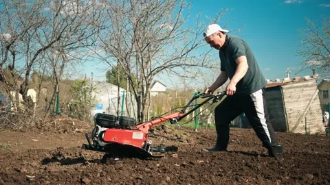 A man prepares the ground with a walk-behind tractor. Stockbeeldmateriaal 162194048