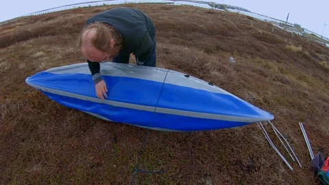 Man prepares for kayaking assembling boat against landscape Video stock 124629783