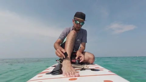 Man prepares for paddleboarding by securing ankle leash to his leg on a SUP Video stock 313844704