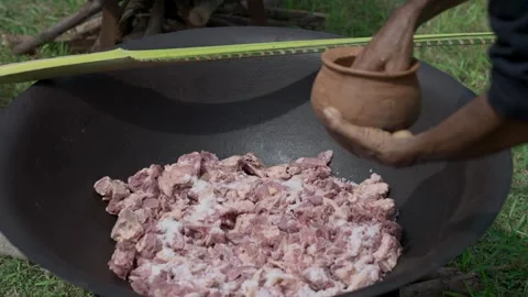 A man prepares pieces of meat to be cooked in a large iron pot Video stock 269484817