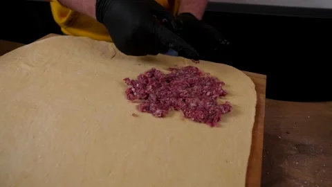 A man prepares a roll of dough stuffed with meat, onions and spices Stock Footage 136830600