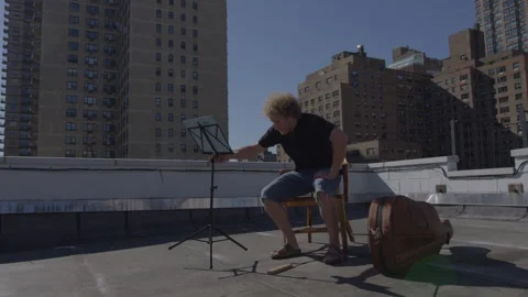 Man prepares for rooftop music session with cello case and stand Stock Footage 312640495