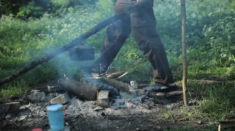 A man prepares tea on a campfire. Checks as a burning fire in early moning Stock Footage 64325870