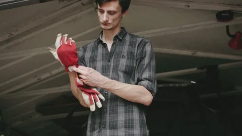 Man prepares to work by putting on red gloves in a garage space during daylight Stock Footage 303806181