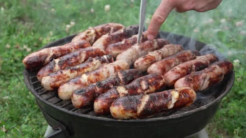 Man preparing and grilling sausages on a charcoal BBQ Stock Footage 338011095