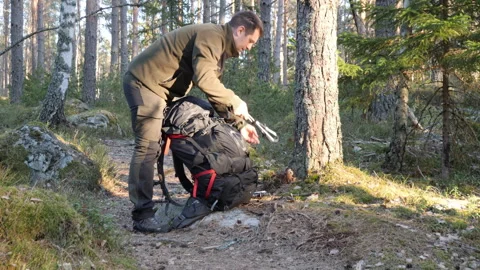 Man preparing backpack on forest trail during sunny outdoor hike Stock Footage 333690857