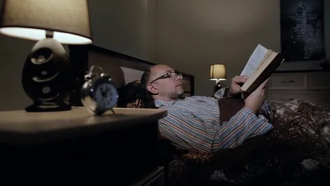A man preparing for bed, reading a book in the bedroom Stock Footage 84740869