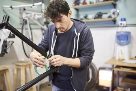 Man preparing a bicycle frame with masking tape to paint it in his workshop. Foto stock