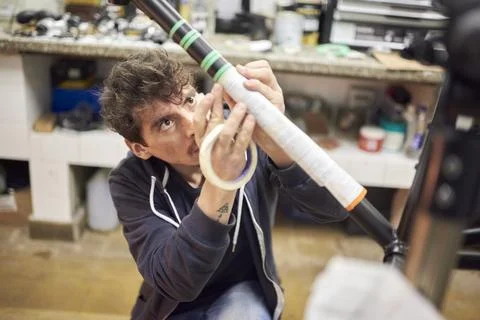Man preparing a bicycle frame with masking tape to paint it in his workshop. Stock Photos
