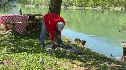 Man Preparing Campfire Near River During Picnic in Countryside, Outdoor Survival Stock Footage 333523052