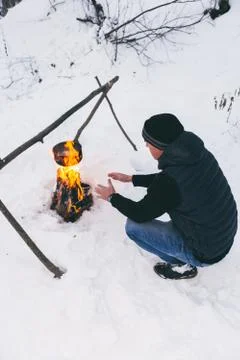 Man is preparing a fire and boiling water for cooking, winter camping. Stock Photos