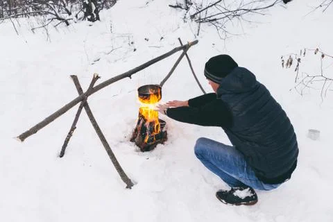 Man is preparing a fire and boiling water for cooking, winter camping. Stock Photos