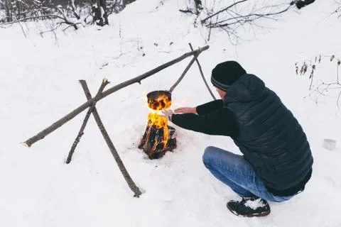 Man is preparing a fire and boiling water for cooking, winter camping. Stock Photos