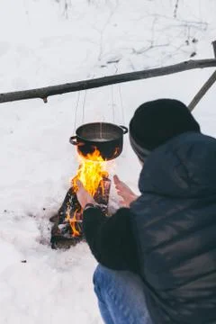 Man is preparing a fire and boiling water for cooking, winter camping. Stock Photos