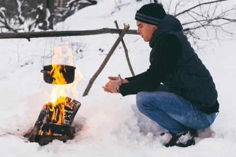 Man is preparing a fire and boiling water for cooking, winter camping. Stock Photos