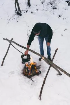 Man is preparing a fire and boiling water for cooking, winter camping. Stock Photos
