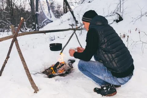 Man is preparing a fire and boiling water for cooking, winter camping. Stock Photos