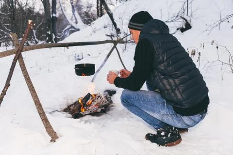 Man is preparing a fire and boiling water for cooking, winter camping. Foto stock