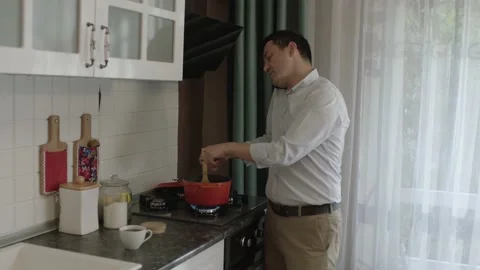 Man preparing food in kitchen and talking on cell phone at the same time. Stock Footage 201338414