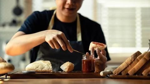 Man preparing a healthy breakfast, spreading raspberry jam on slice of bread Stock Photos