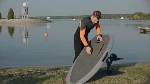 Man preparing his hydrofoil surfboard at the lake shore on a sunny day Stock-Footage 166546540