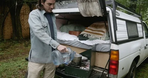 Man preparing a meal and pouring water into a camp pot on the back of his truck Stock Footage 80809552