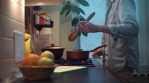 Man preparing meal in pan on stove in kitchen. stirs wooden spoon Stock-Footage 83044868