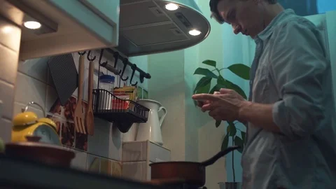 Man preparing meal in pot on stove in kitchen, using smartphone Stock Footage 83088094