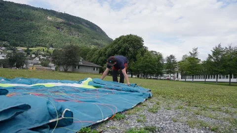 Man preparing paraglider on grassy field with Norway mountains in the background 스톡 동영상 308215780