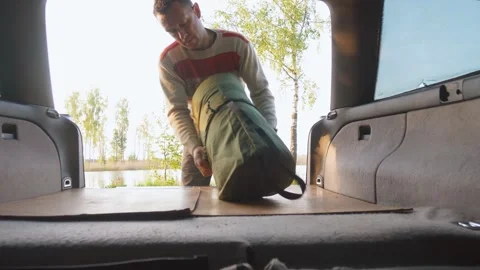 Man preparing a sleeping bag inside car for a camping road trip Stock Footage 322667668