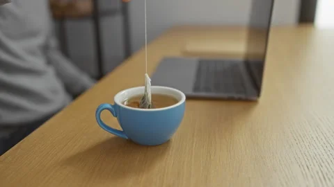 Man preparing tea in a blue cup on a wooden office desk near a laptop, high.. Stock Footage 302486185