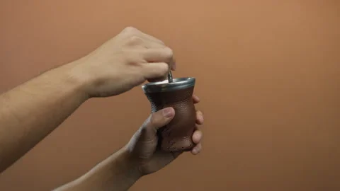 Man preparing traditional mate drink using a brown leather gourd against an.. Stock Footage 313911115